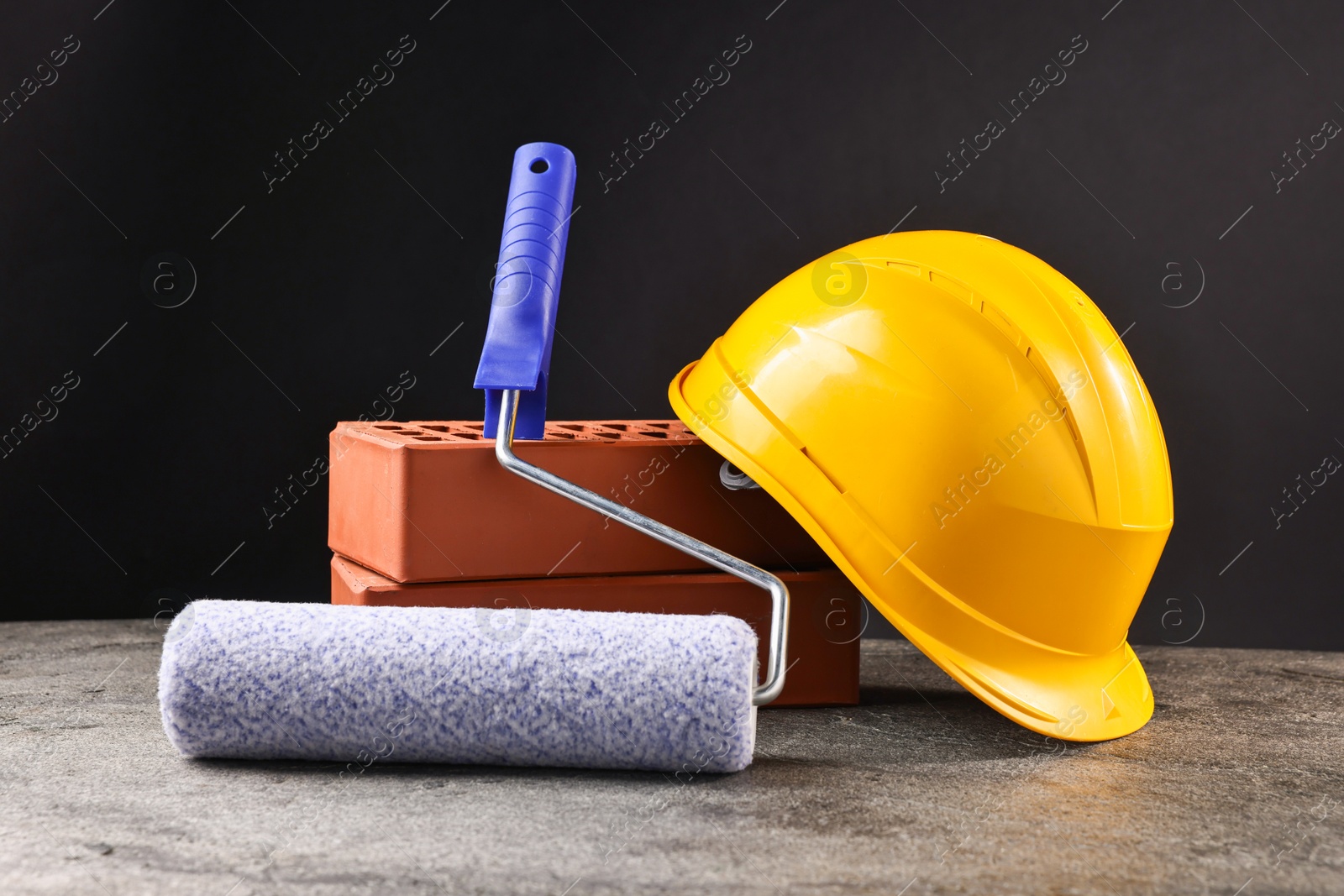 Photo of Bricks, hardhat and paint roller on grey table