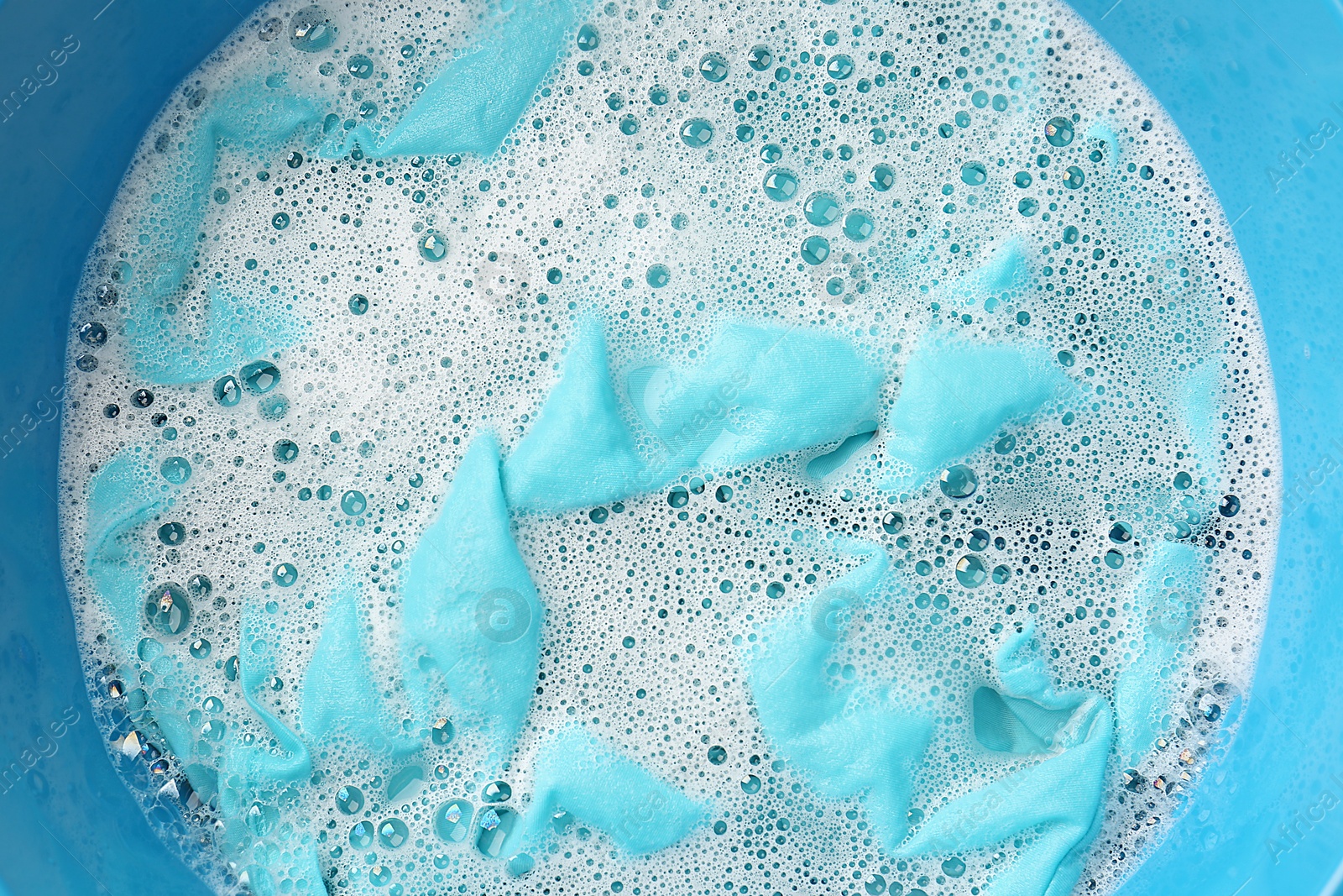 Photo of Turquoise clothes soaked in water before washing, top view