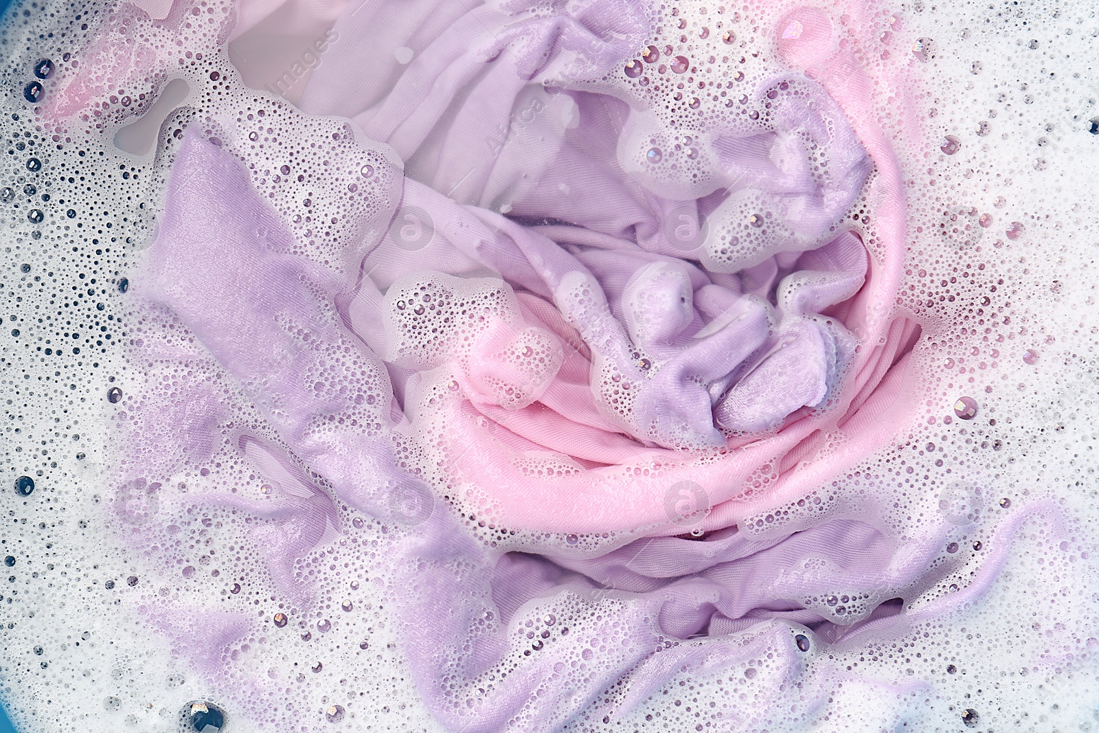 Photo of Colorful clothes soaked in water before washing, top view