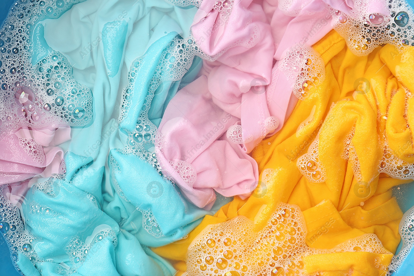 Photo of Colorful clothes soaked in water before washing, top view