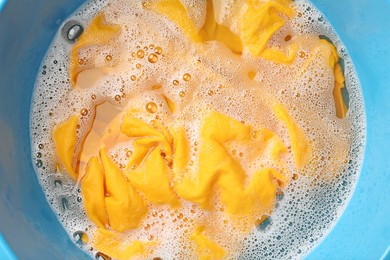 Photo of Yellow clothes soaked in water before washing, top view