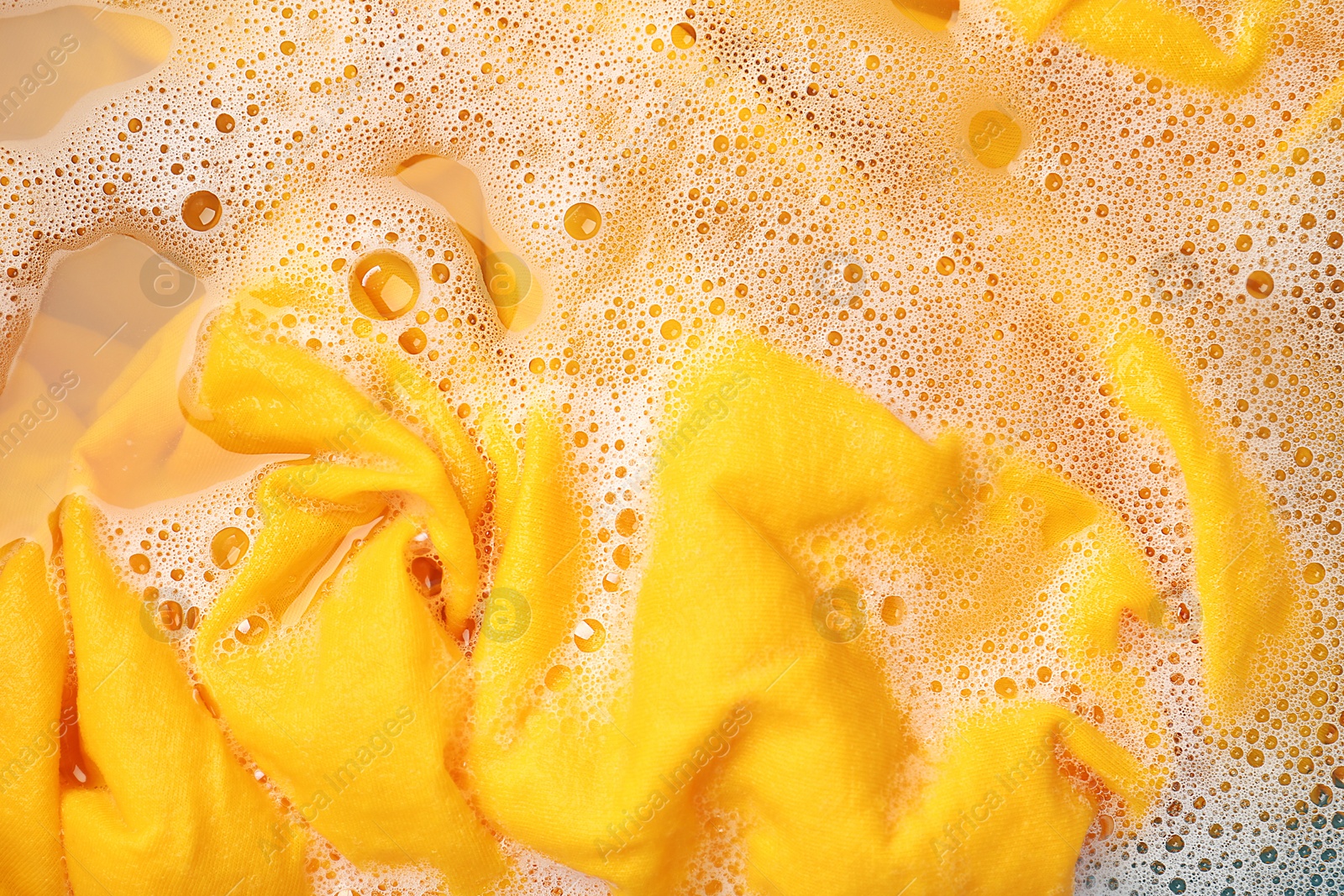 Photo of Yellow clothes soaked in water before washing, top view