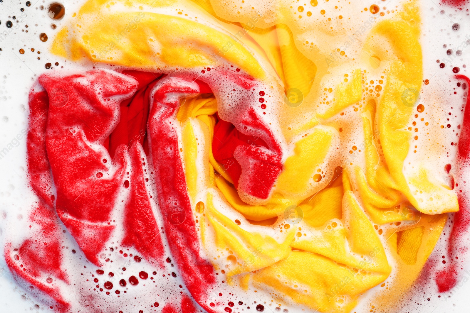 Photo of Colorful clothes soaked in water before washing, top view