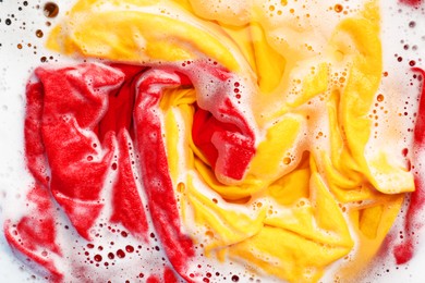 Photo of Colorful clothes soaked in water before washing, top view