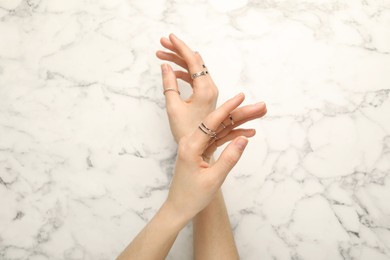 Photo of Woman wearing beautiful rings at white marble table, top view