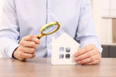 Photo of Real estate agent looking at house figure through magnifying glass at wooden table in office, closeup. Home appraisal