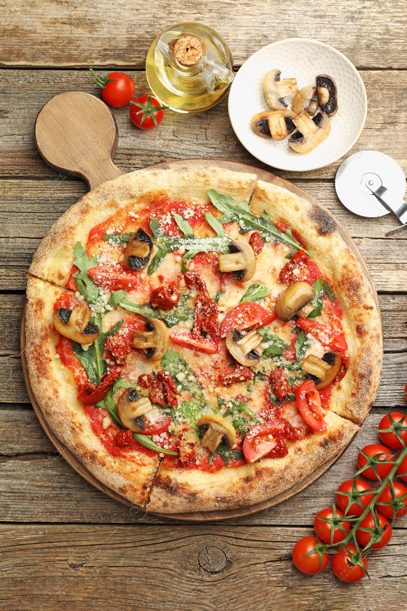 Photo of Tasty pizza with mushrooms, tomatoes, arugula and cutter on wooden table, flat lay