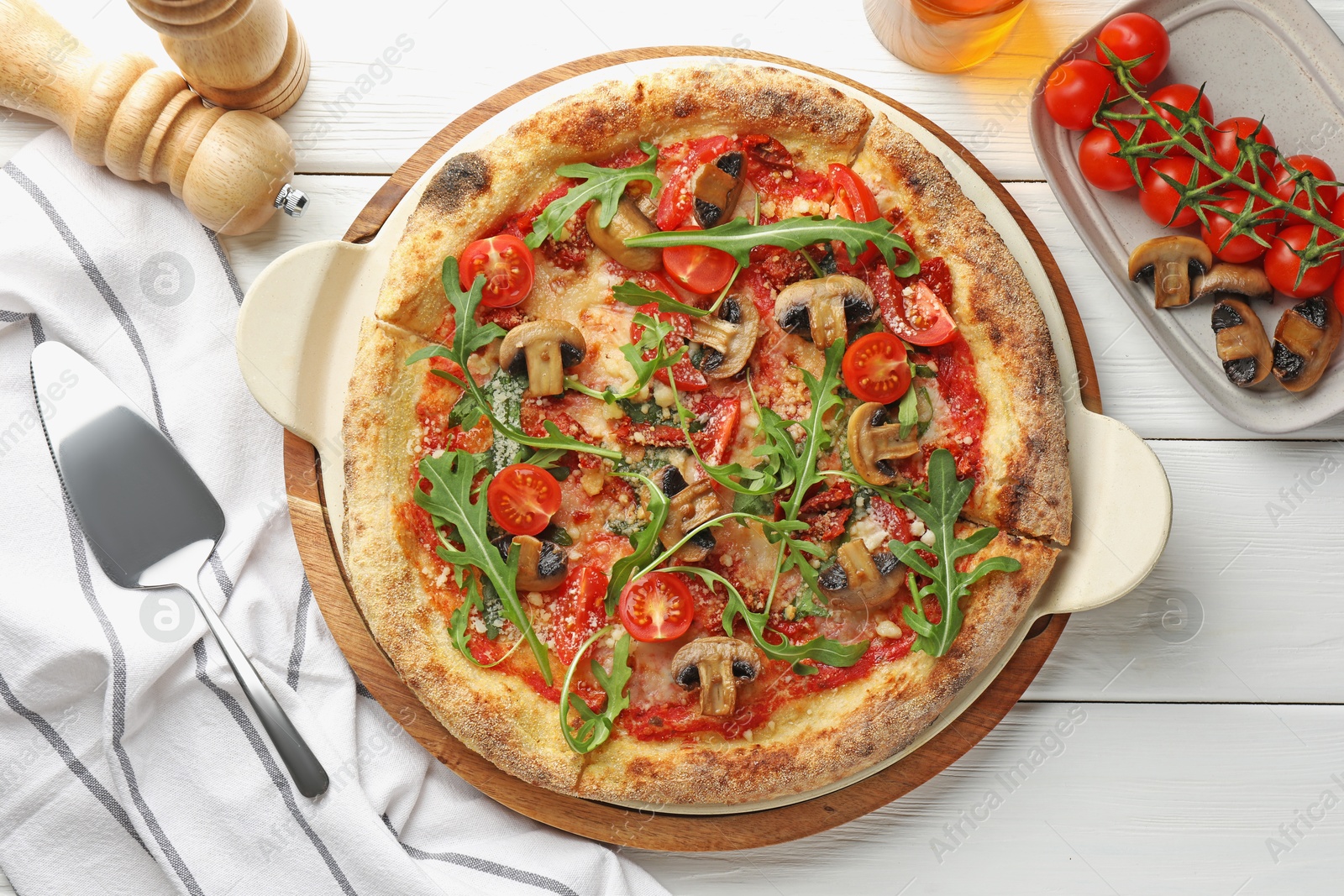 Photo of Tasty pizza with mushrooms, tomatoes, arugula and server on white wooden table, flat lay