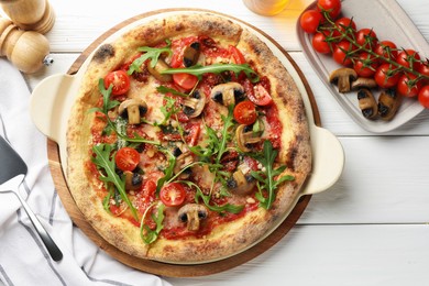 Photo of Tasty pizza with mushrooms, tomatoes, arugula and server on white wooden table, flat lay