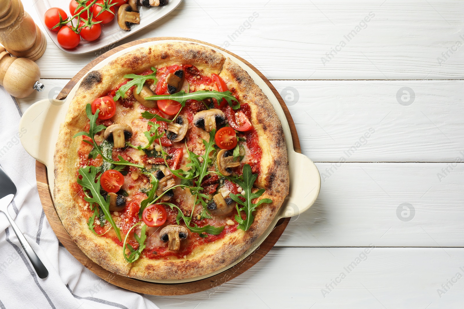 Photo of Tasty pizza with mushrooms, tomatoes, arugula and server on white wooden table, flat lay. Space for text