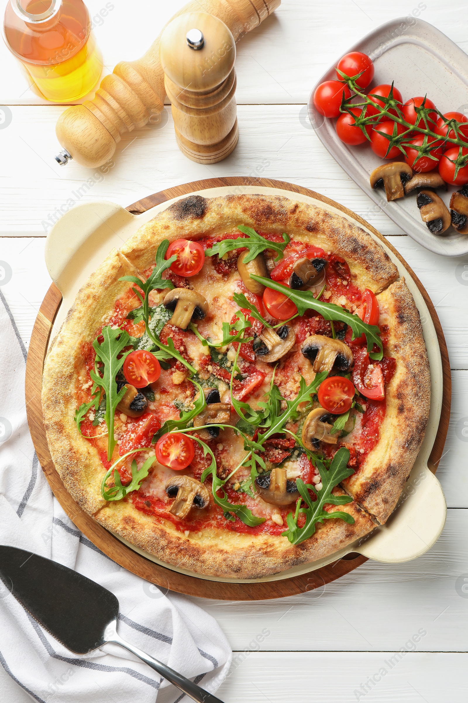 Photo of Tasty pizza with mushrooms, tomatoes, arugula and server on white wooden table, flat lay