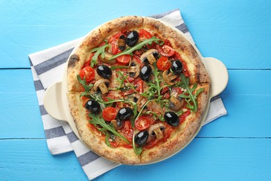 Tasty pizza with mushrooms, black olives and arugula on light blue wooden table, top view