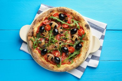 Tasty pizza with mushrooms, black olives and arugula on light blue wooden table, top view