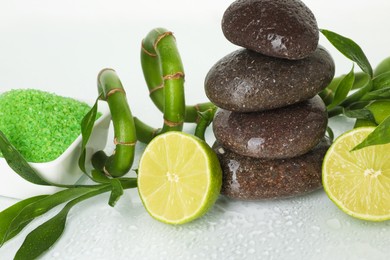 Photo of Spa composition with fresh limes, sea salt, massage stones and bamboo on wet surface, closeup