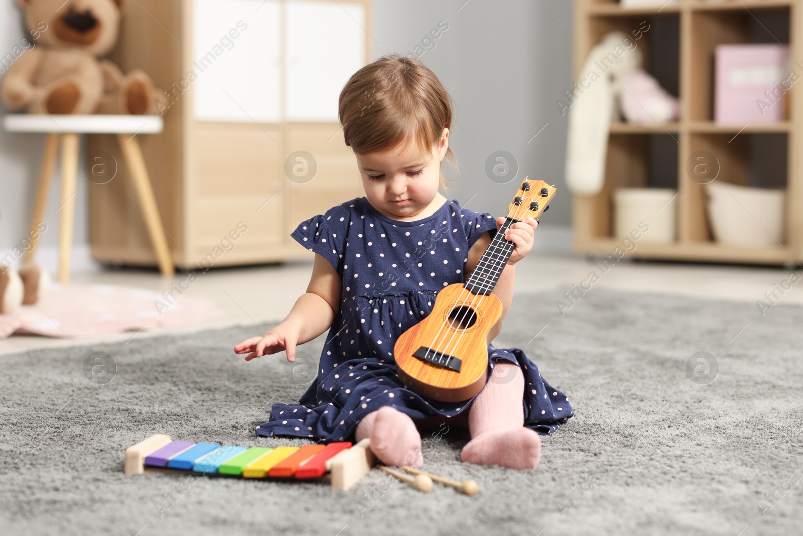 Photo of Cute little girl playing with toy guitar on floor at home