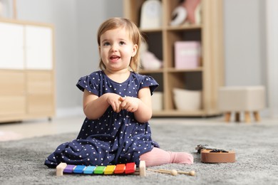 Photo of Cute little girl playing with toy musical instruments on floor at home