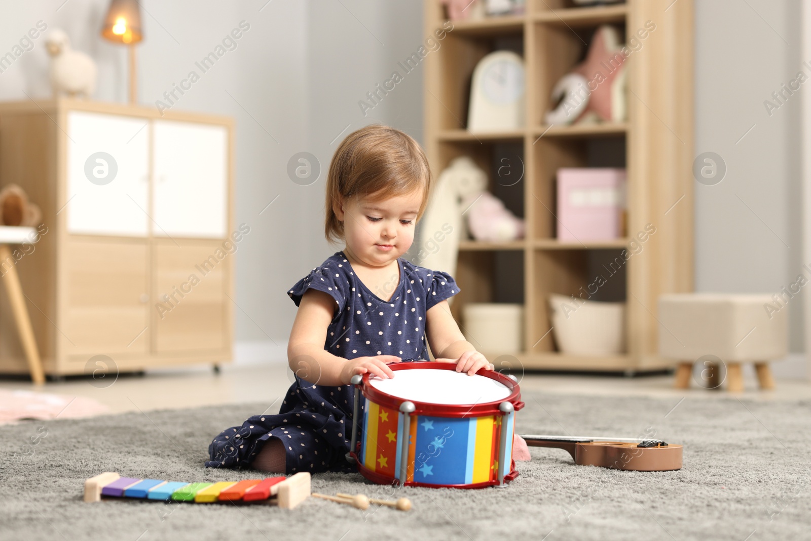 Photo of Cute little girl playing with toy drum on floor at home