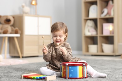 Photo of Cute little girl playing with toy musical instruments on floor at home