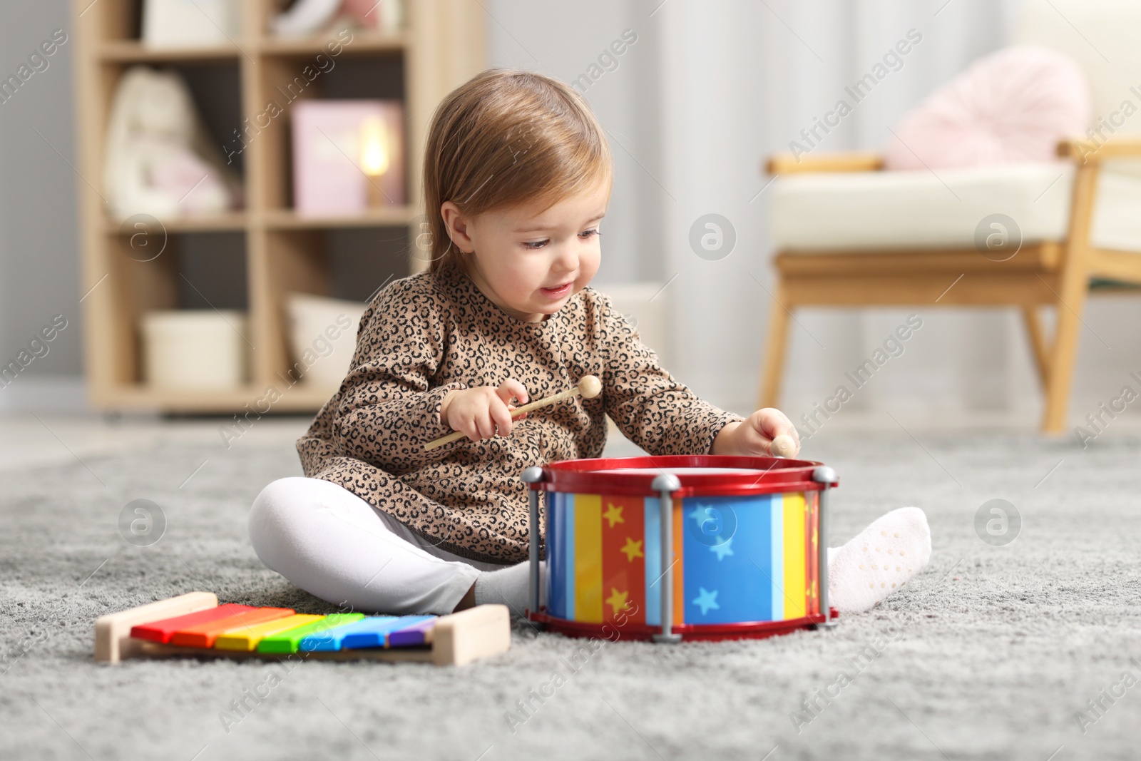 Photo of Cute little girl playing with toy drum on floor at home