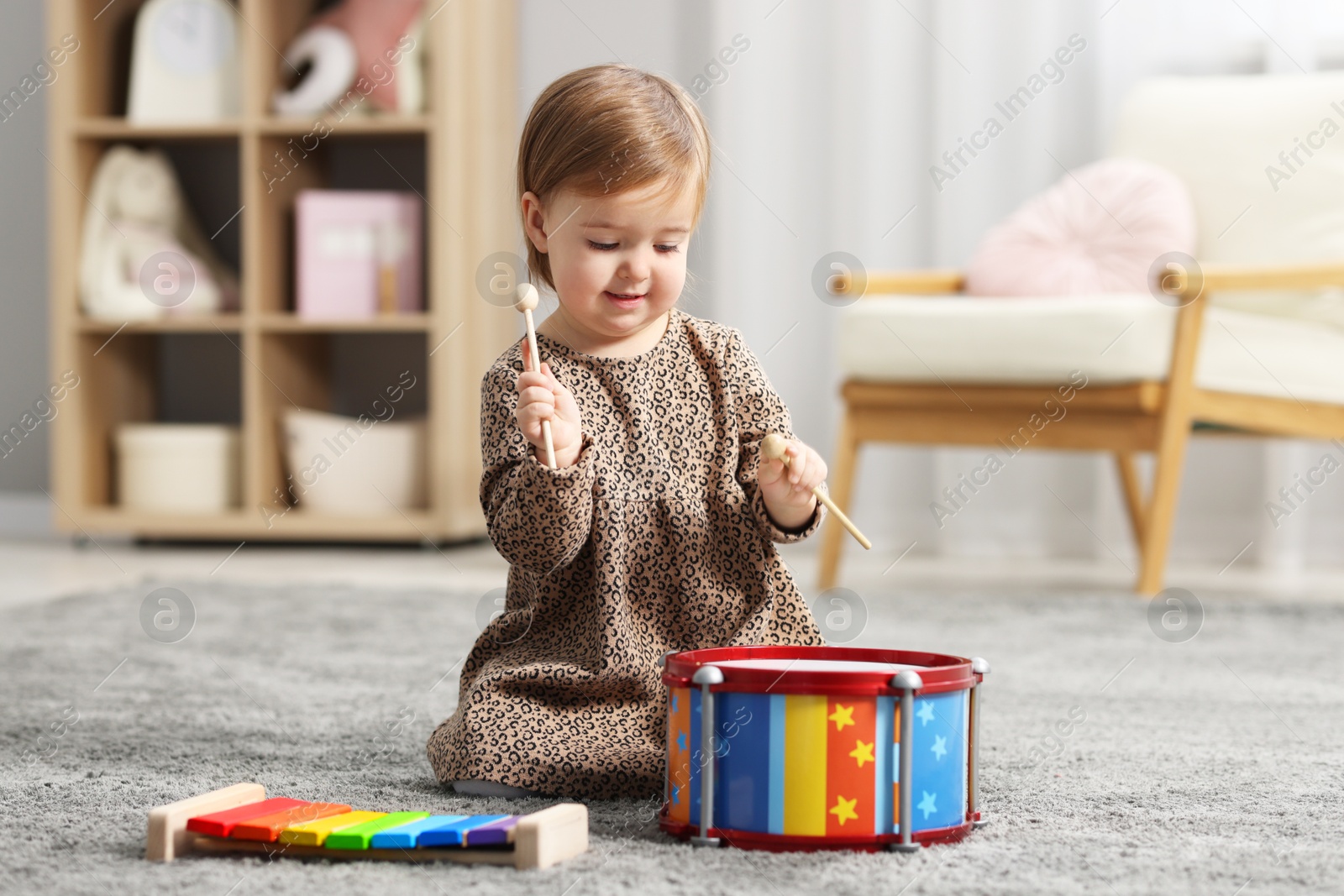 Photo of Cute little girl playing with toy drum on floor at home