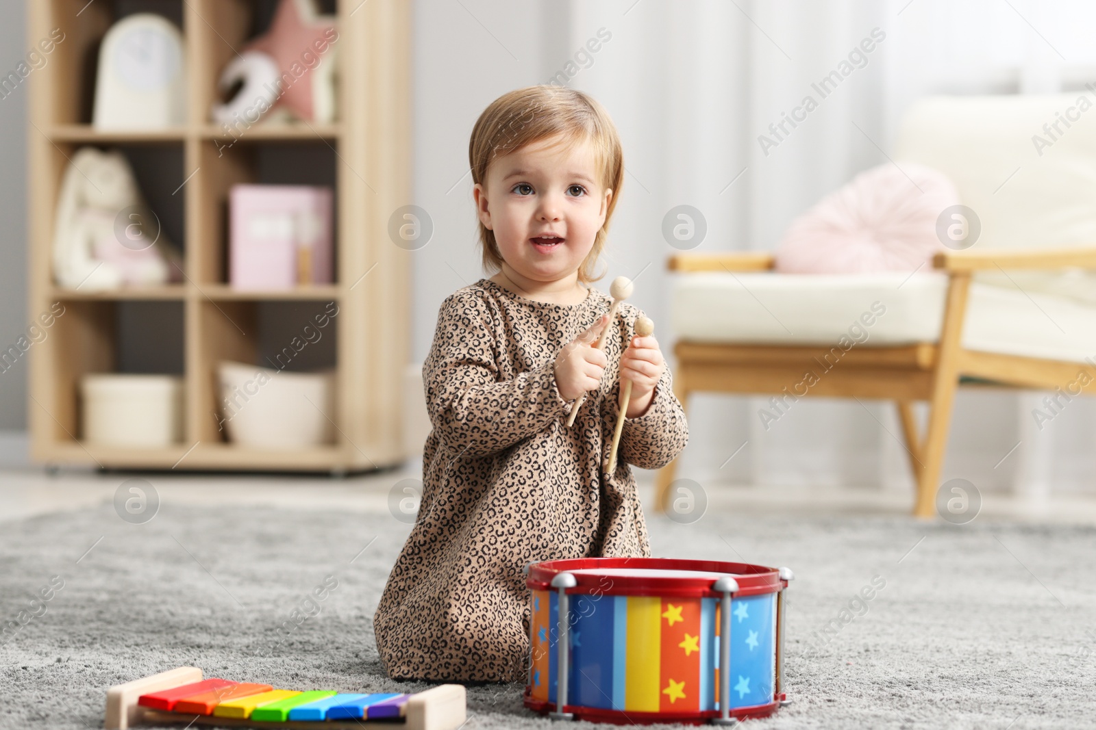 Photo of Cute little girl playing with toy drum on floor at home