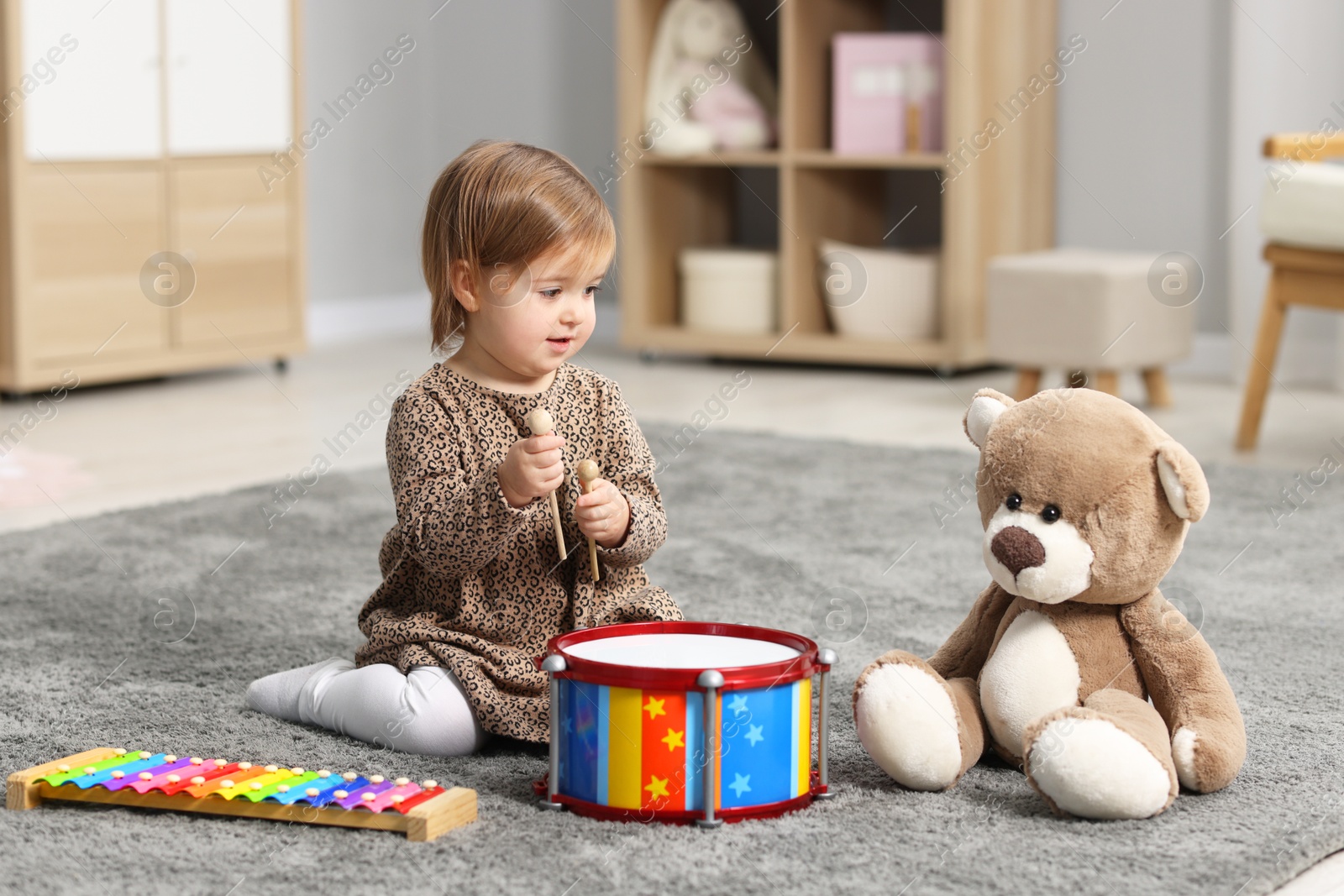 Photo of Cute little girl playing with toy musical instruments on floor at home