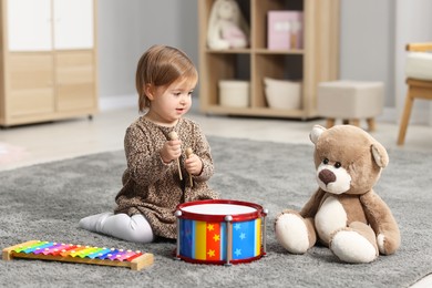 Photo of Cute little girl playing with toy musical instruments on floor at home