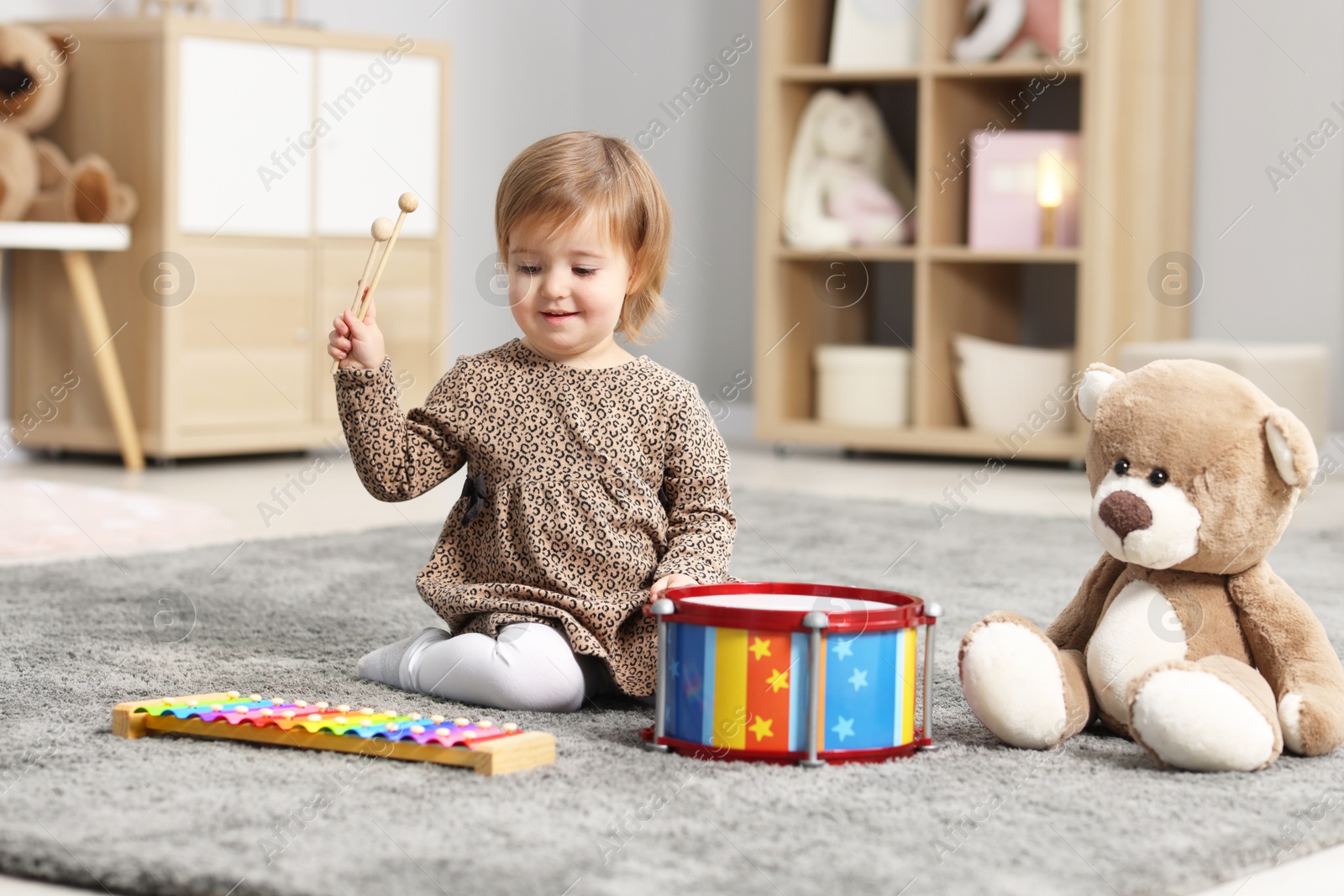 Photo of Cute little girl playing with toy musical instruments on floor at home