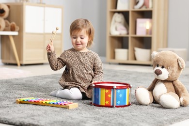 Photo of Cute little girl playing with toy musical instruments on floor at home