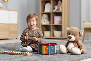 Photo of Cute little girl playing with toy musical instruments on floor at home