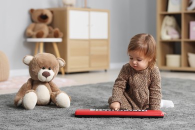 Photo of Cute little girl playing with toy piano at home