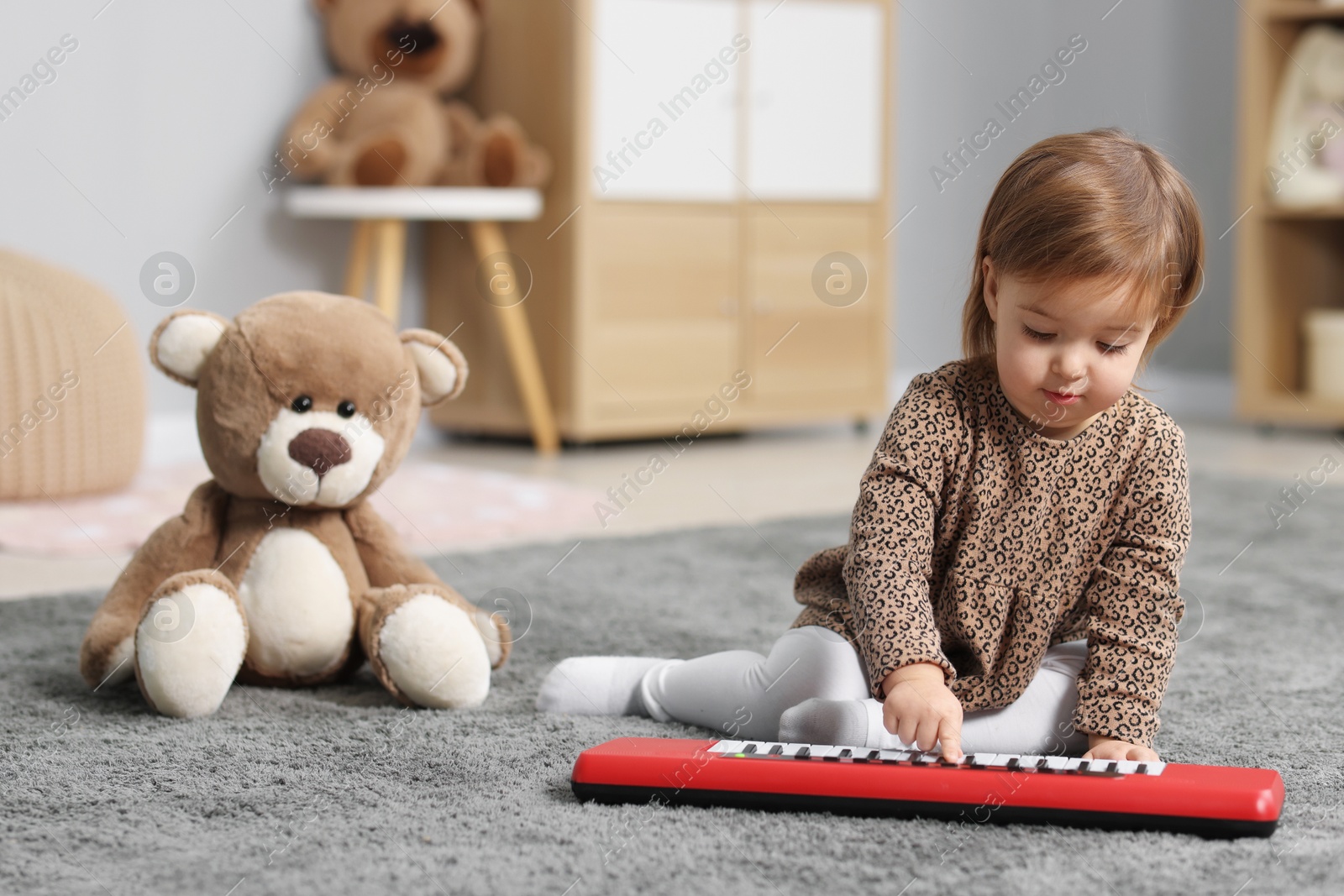 Photo of Cute little girl playing with toy piano at home