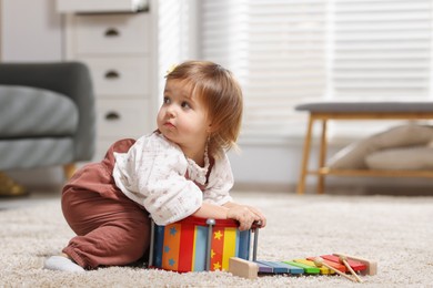 Photo of Cute little girl playing with toy drum on floor at home, space for text