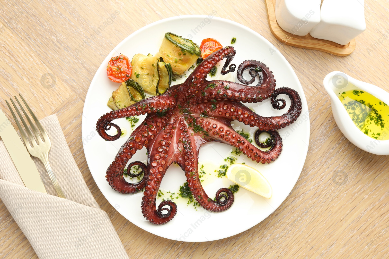 Photo of Fried octopus with herb sauce, vegetables and lemon on wooden table, flat lay