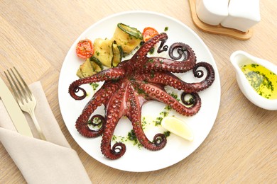 Fried octopus with herb sauce, vegetables and lemon on wooden table, flat lay