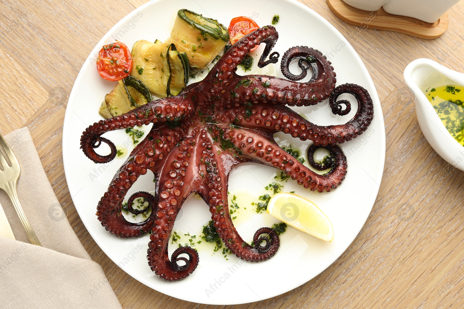 Photo of Fried octopus with herb sauce, vegetables and lemon on wooden table, flat lay