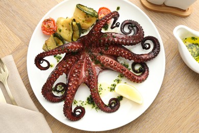 Fried octopus with herb sauce, vegetables and lemon on wooden table, flat lay