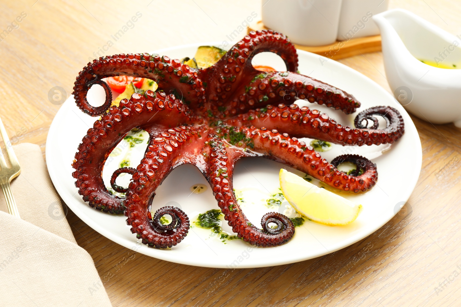 Photo of Fried octopus with herb sauce and lemon on wooden table, closeup