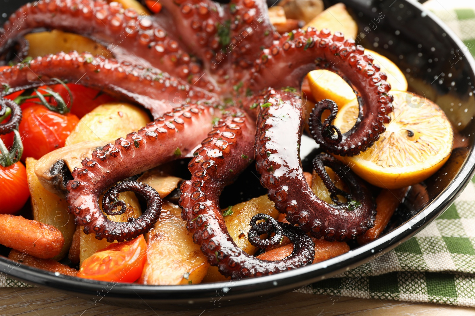 Photo of Fried octopus with lemon and vegetables in pan on wooden table, closeup