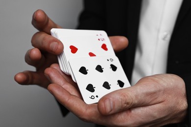 Photo of Illusionist shuffling playing cards on grey background, closeup