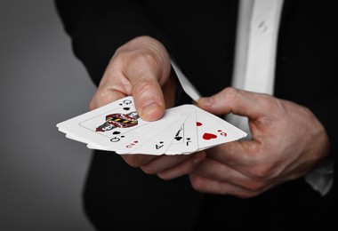 Illusionist hiding one playing card up his sleeve while showing deck on grey background, closeup