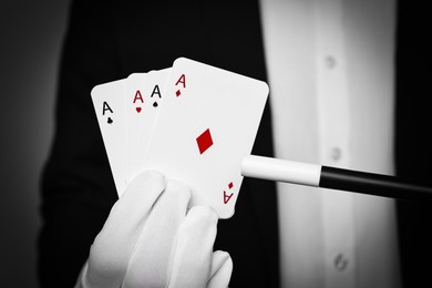 Photo of Illusionist pointing magic wand on playing cards against grey background, closeup