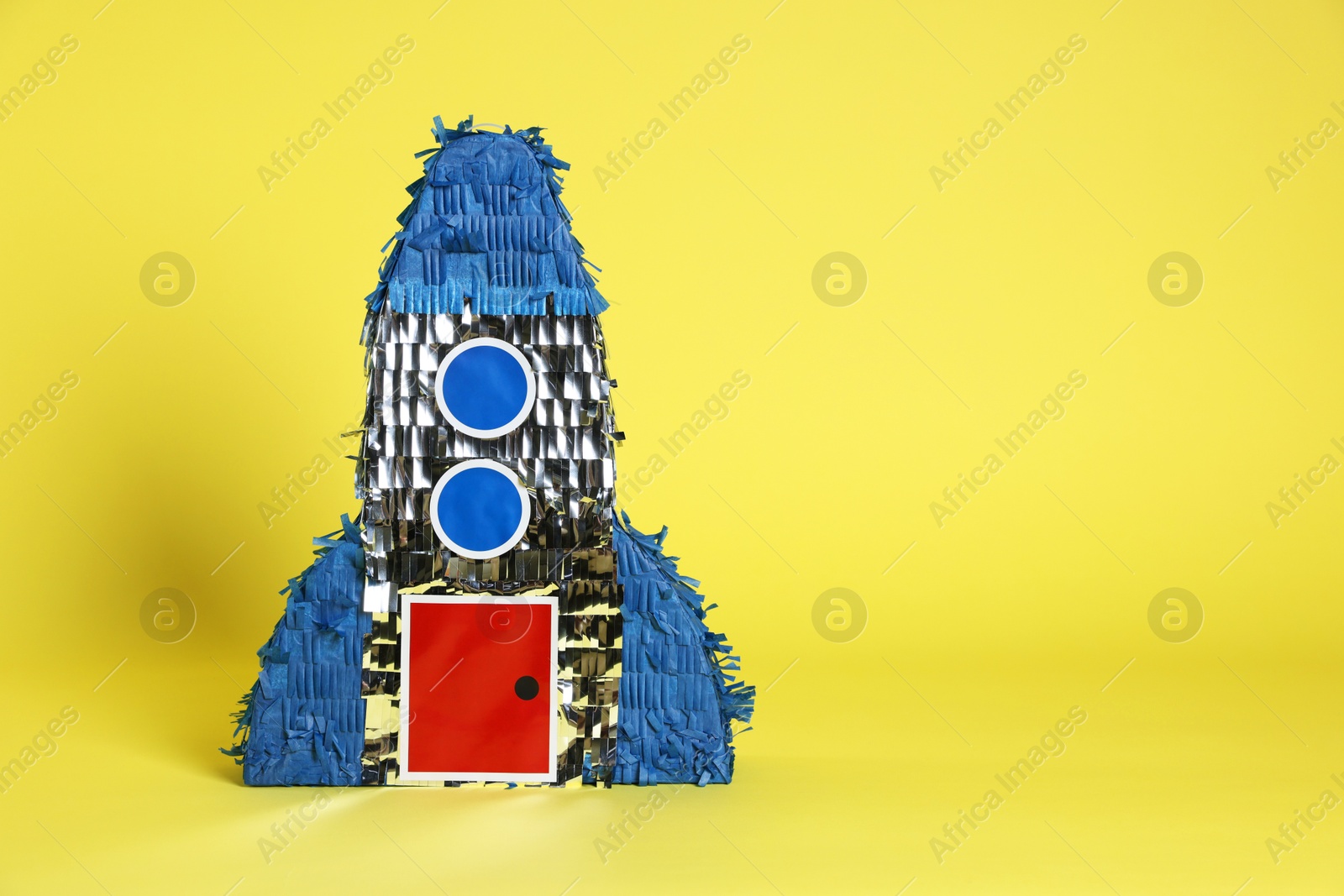 Photo of Rocket shaped pinata on yellow background, space for text