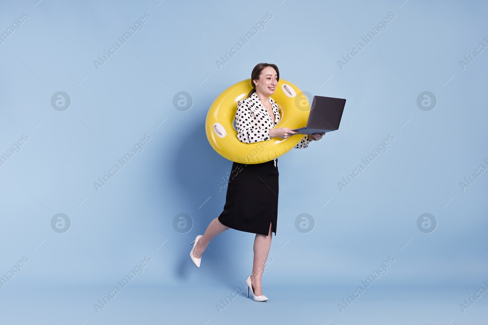 Photo of Businesswoman with inflatable ring and laptop on light blue background