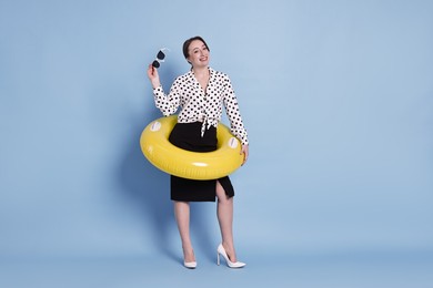 Businesswoman with inflatable ring and sunglasses on light blue background