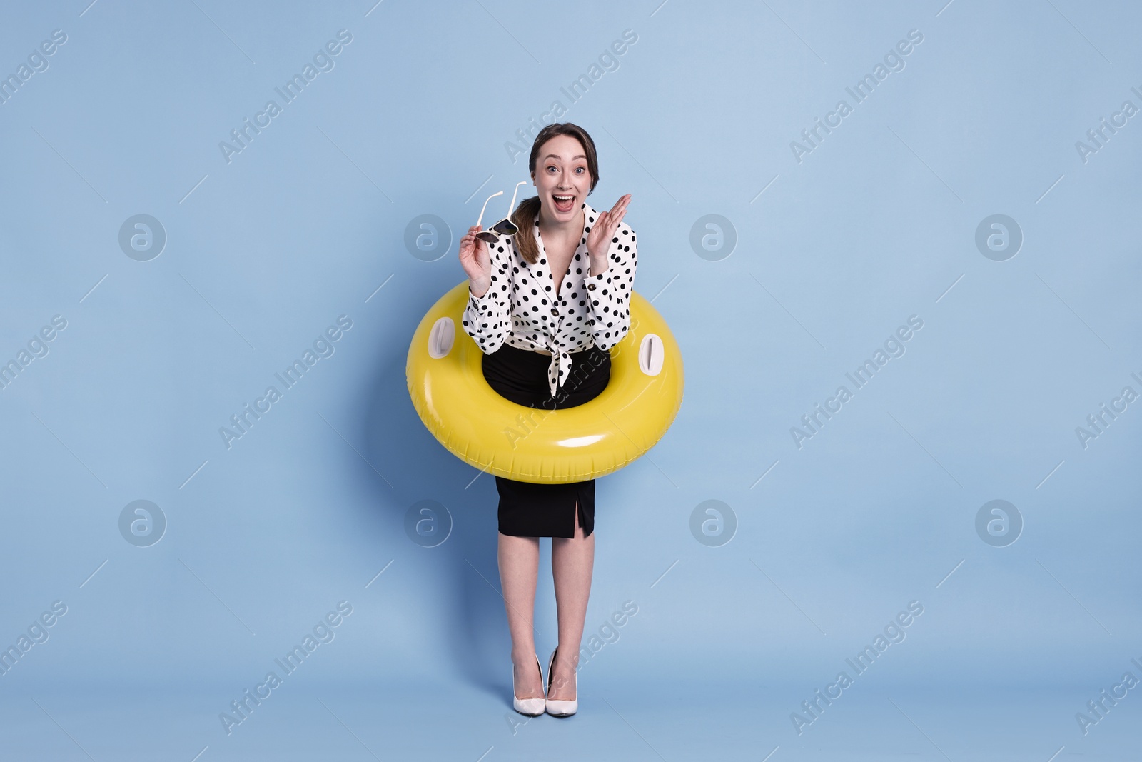 Photo of Businesswoman with inflatable ring and sunglasses on light blue background