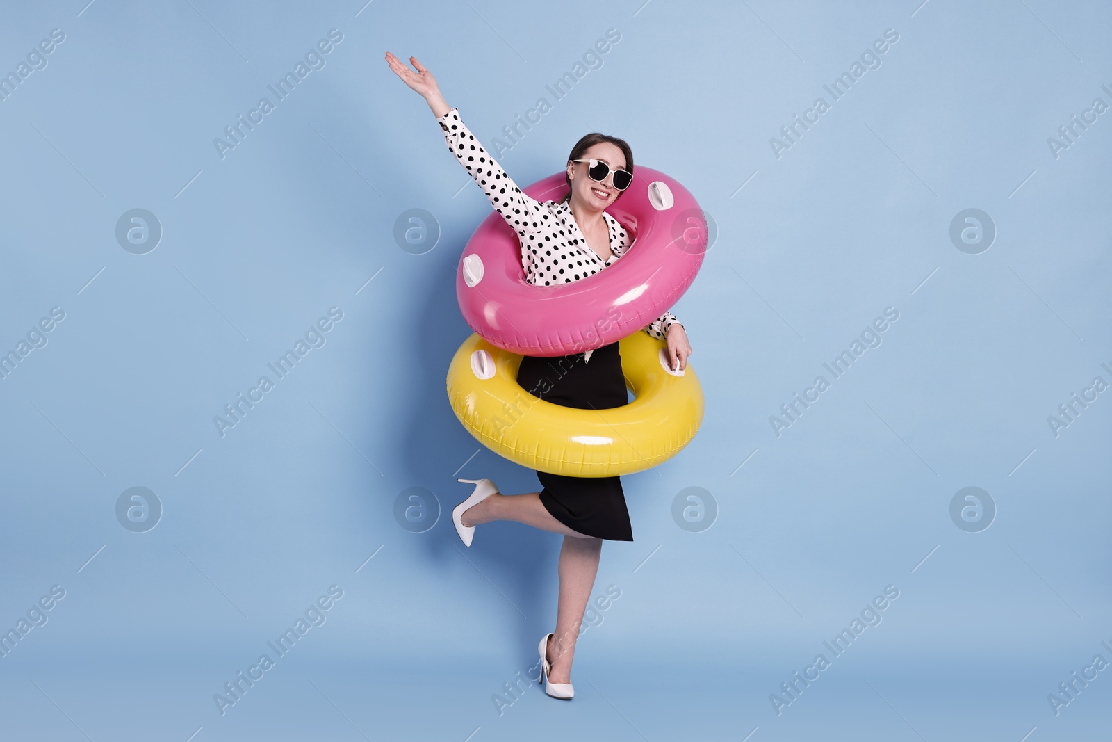 Photo of Businesswoman with inflatable rings and sunglasses on light blue background