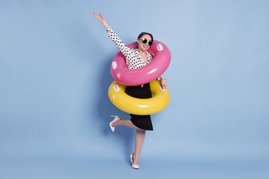 Photo of Businesswoman with inflatable rings and sunglasses on light blue background