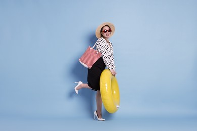 Photo of Businesswoman with inflatable ring, straw hat, bag and sunglasses on light blue background