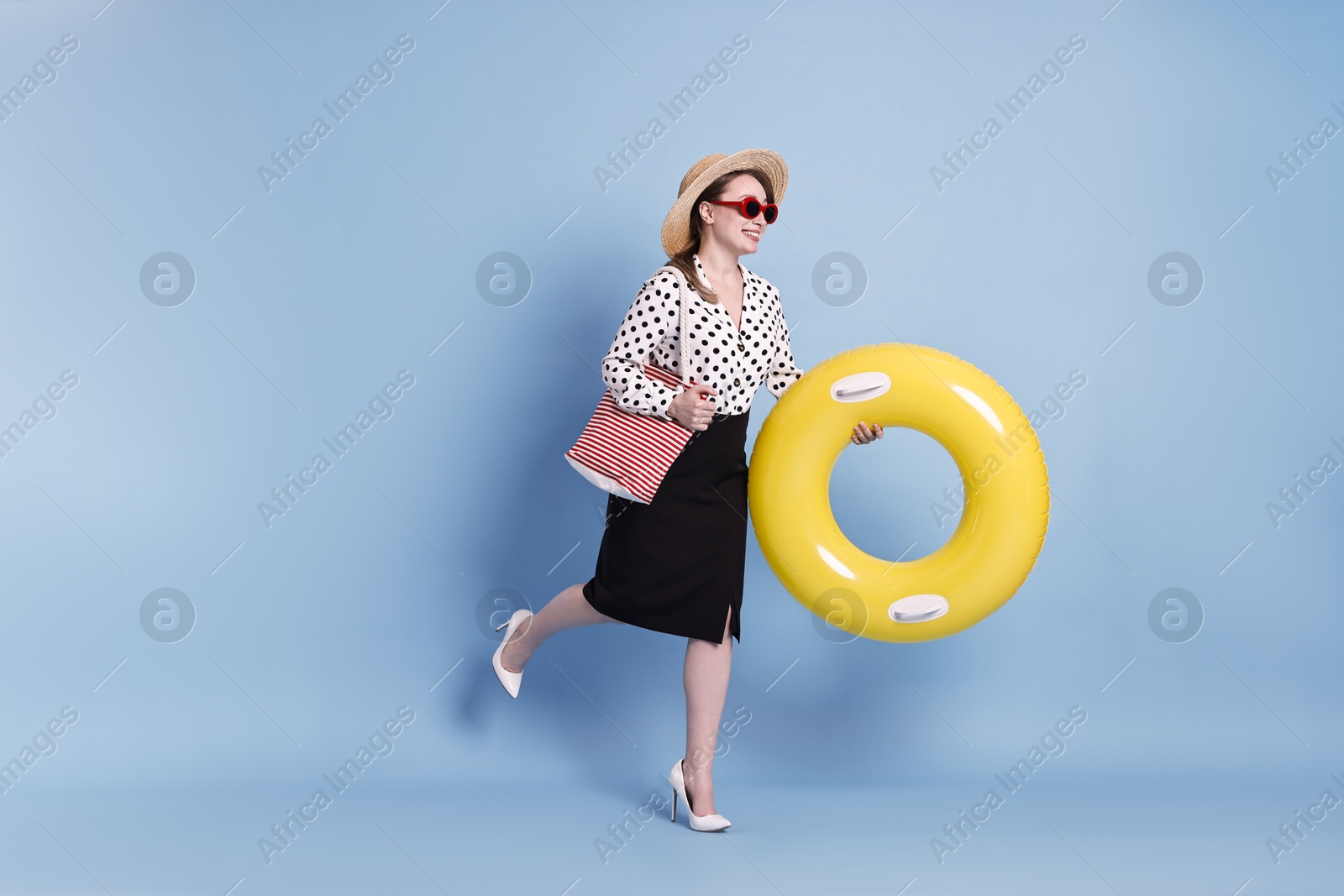 Photo of Businesswoman with inflatable ring, straw hat, bag and sunglasses on light blue background